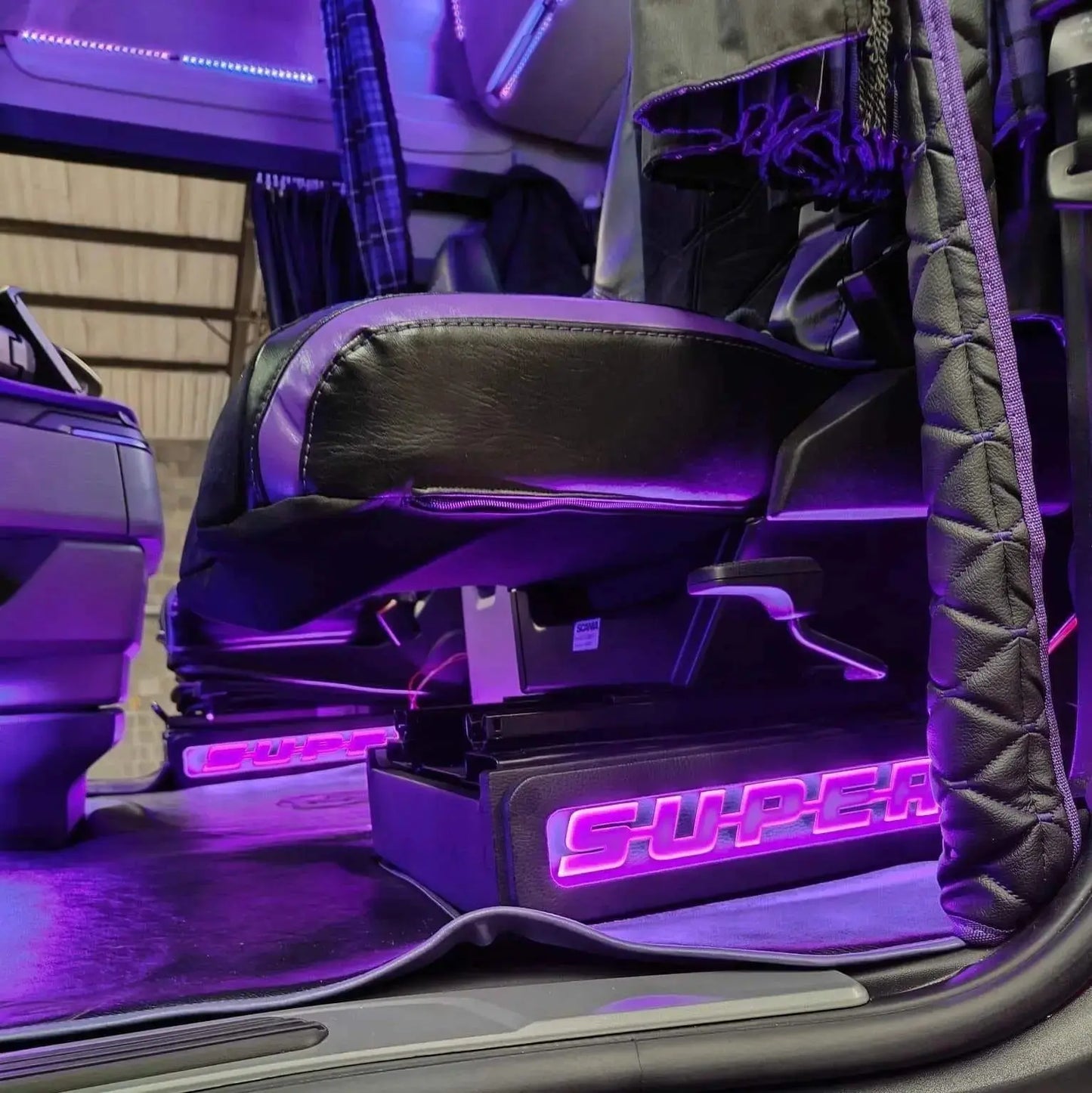 Scania Super Truck LED Seat Bases (Side Lit) in purple ambient light, showing leather trim, SUPER logo, and accessories within the cab.
