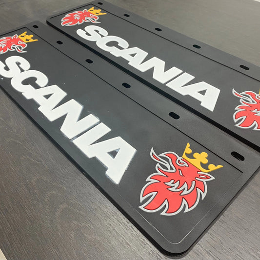 Mud flaps made by TLD featuring SCANIA branding and red crowned griffin logos, laid side by side on a wooden surface.