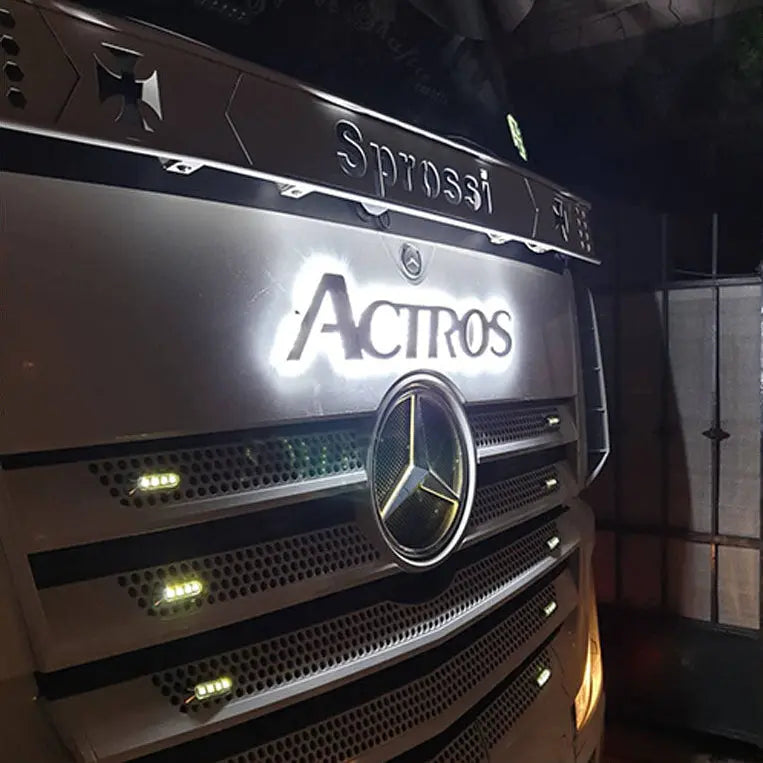 Close-up of a Mercedes Actros truck showcasing the illuminated Actros grille badge, highlighting its LED back-lit feature prominently above the grille.