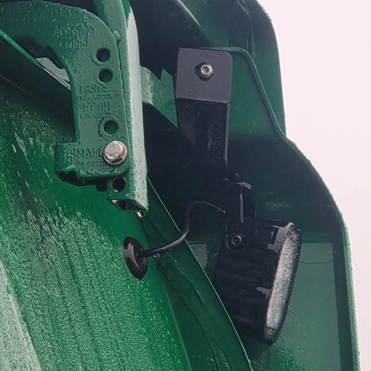 Close-up of Scania Next Gen Reduced Wind Kit Work Light Mounts, showing adjustable hinge and LED mount, wet from rain.