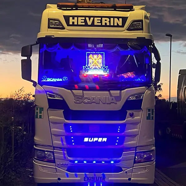 Front view of Scania S-series with 'SUPER' 3D Light badge, blue LED accents, and illuminated West Ham United crest, showcasing vibrant blue interior lighting.