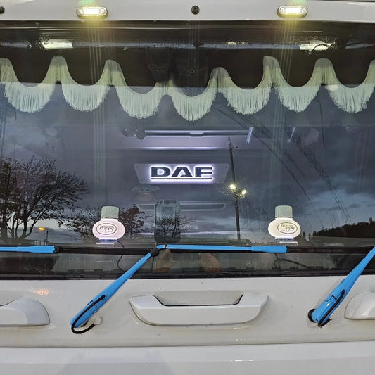 DAF 3D Truck Light Board on truck windshield, featuring an illuminated badge, cream fringe valance, Poppy air-fresheners, and blue wiper arms.
