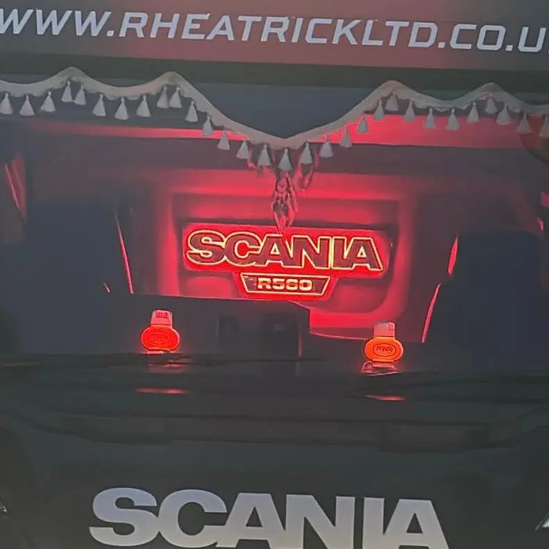 Scania R-series cab featuring TLD's Scania Infill Panel LED Truck Light Board, showcasing illuminated SCANIA R560 badge and tassel fringe on windshield.