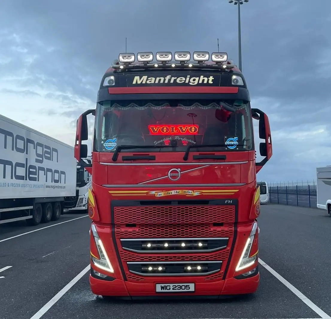 Volvo FH truck with Manfreight visor, showcasing a R/S Series Truck Light Board (Scania Compatible) inside, featuring bold VOLVO letters and decorative red curtains.