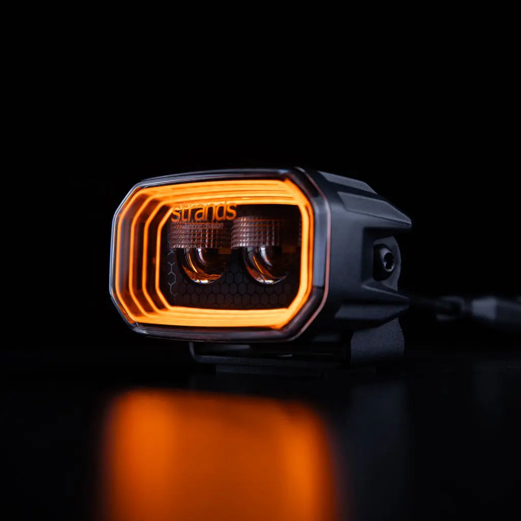 |STRANDS| FOR9T NO-GLARE WORKLIGHT 31W, showcasing dual-lens LED optics with a glowing orange halo, designed for reduced glare and enhanced night visibility.