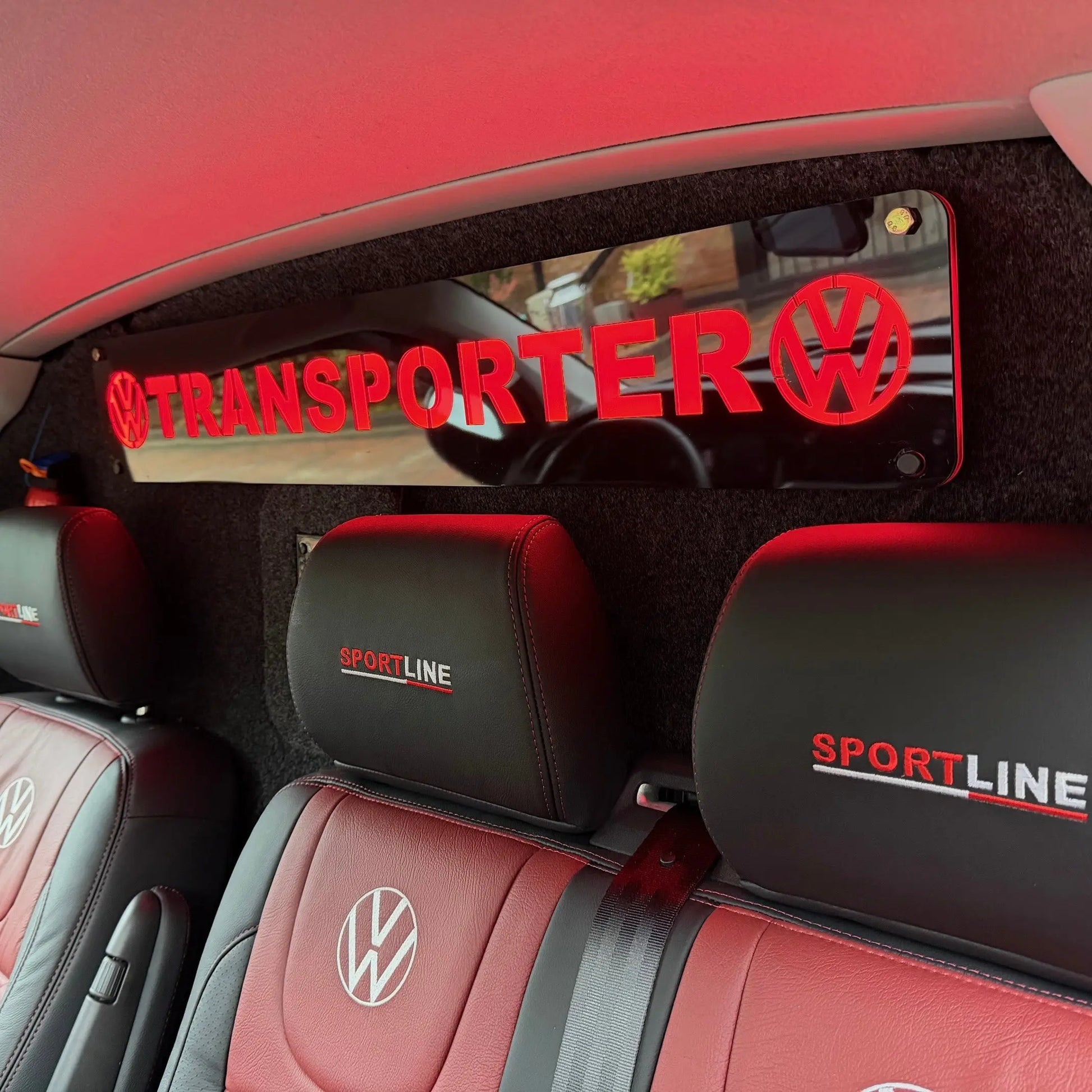 VW Transporter Bulkhead Sign 900x150mm shown above red-and-black leather seats, features back-lit TRANSPORTER with VW logos, enhancing van interior with bright, stylish signage.