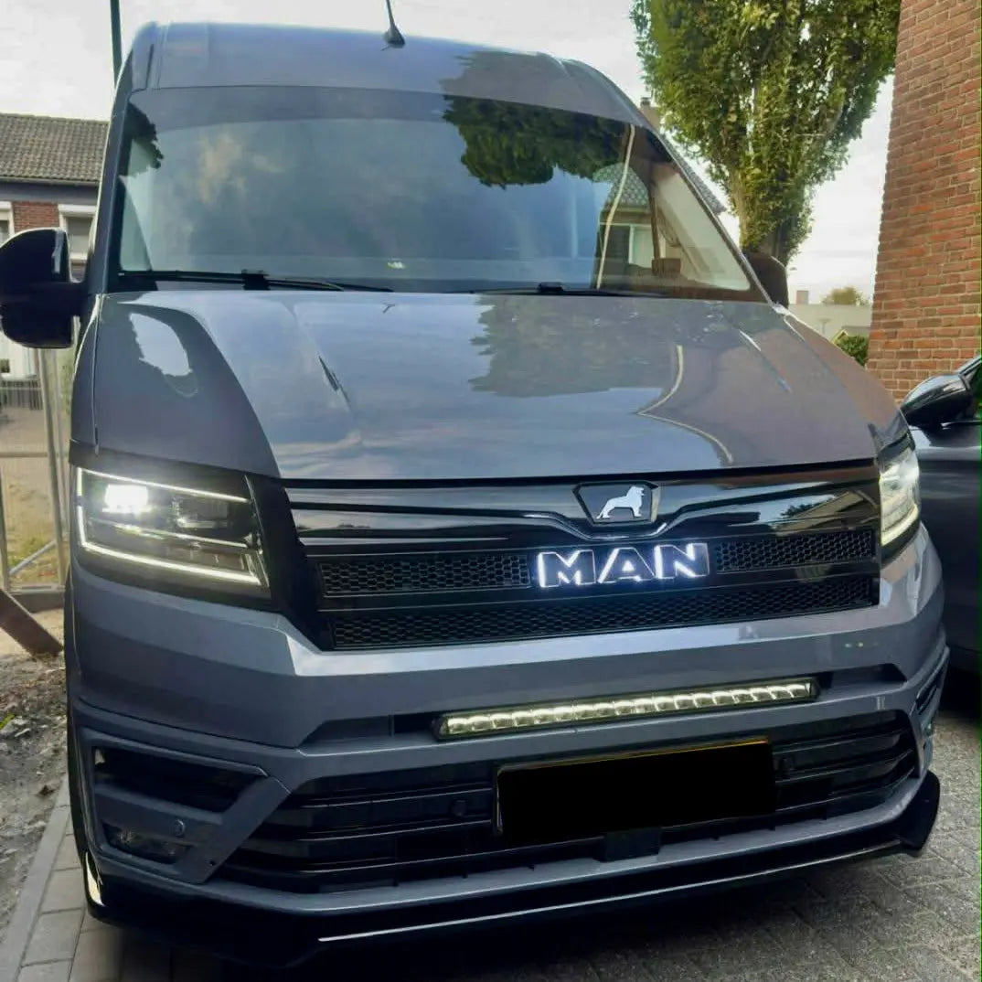MAN TGE Grille Badge LED Back-Lit on dark-grey van, illuminated headlights, grille with MAN badge, light bar in bumper, parked on paved driveway.