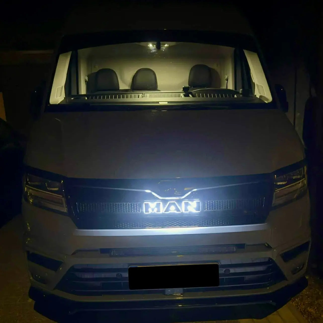 Front view of a white MAN van at night featuring the illuminated MAN TGE Grille Badge Led Back-Lit, highlighting the brand logo in the grille.