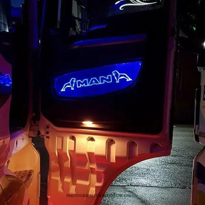 Man Tgx Led Back-Lit Custom Interior Door Panels with blue MAN logo and lion silhouettes, illuminating a wet pavement from a truck door panel at night.
