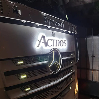 Close-up of a Mercedes Actros Grille Badge LED Back-Lit on a parked truck, featuring illuminated Actros and personalized Sprossi name in low light.
