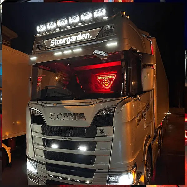 Scania R/S Series Truck Light Board on a white Scania semi-truck, showcasing bright auxiliary lights and a glowing red V8 emblem, enhancing cabin style.