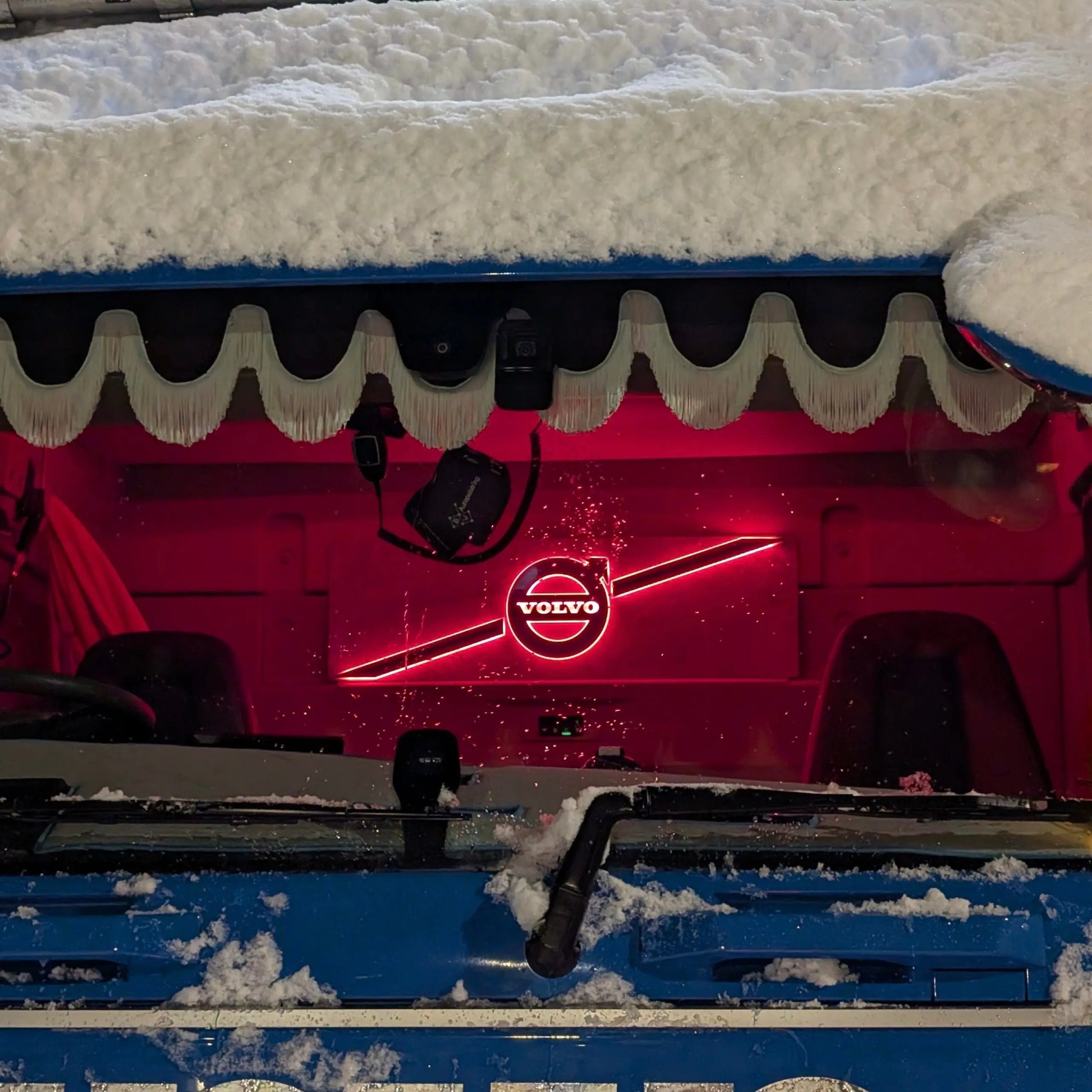 Volvo Badge LED Truck Light Board by TLD glowing red inside snow-covered blue Volvo truck cab, casting a warm light over the interior.