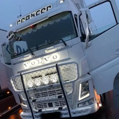 White Volvo truck with aftermarket grille guard featuring four round LED lights. Highlight: Volvo Grille Badge Led Back-Lit visible on the grille.