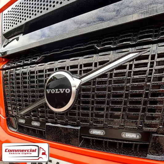 Close-up of Volvo truck grille with Aero Lower Grill Light Bar/Channel Kit, highlighting stainless steel design, LED compatibility, and Commercial Vehicle Lights logo.