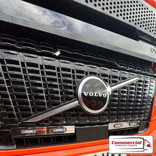 Close-up of a Volvo truck grille featuring the Aero Lower Grill Light Bar/Channel Kit with aftermarket LED marker lights, emphasizing stainless steel construction and compatibility with flush fit LED lights.