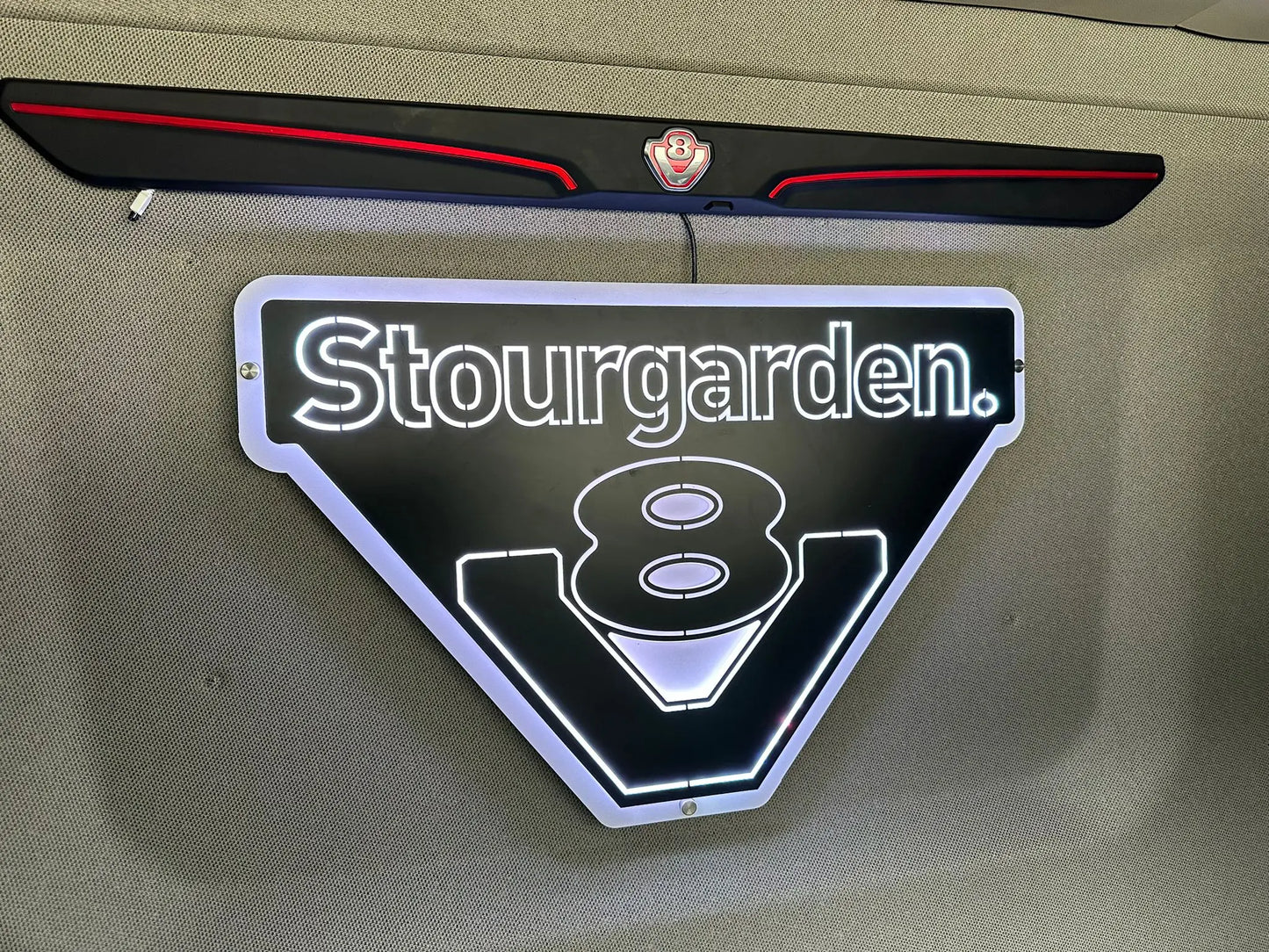 Wall-mounted MAN 3D Truck Light Board with backlit Stourgarden. text, LED-outlined stylized 8 and bold V shape, featuring an illuminated design.