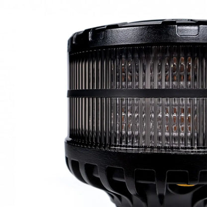 Close-up of Smoked Warning Beacon LED X-SPIDER with ribbed clear lens, revealing orange LEDs inside, mounted on black housing.